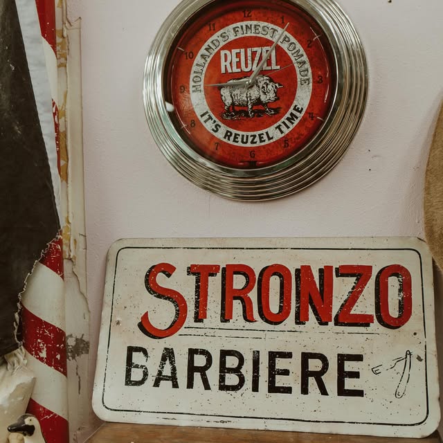 Vintage Stronzo Barbiere sign and Reuzel clock on the shop wall